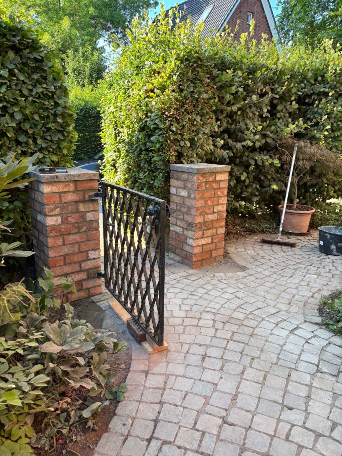 Neu gemauerte Klinker-Säulen mit eingepasstem Metalltor im Eingangsbereich; aufgewerteter und klar strukturierter Zugang nach der Sanierung