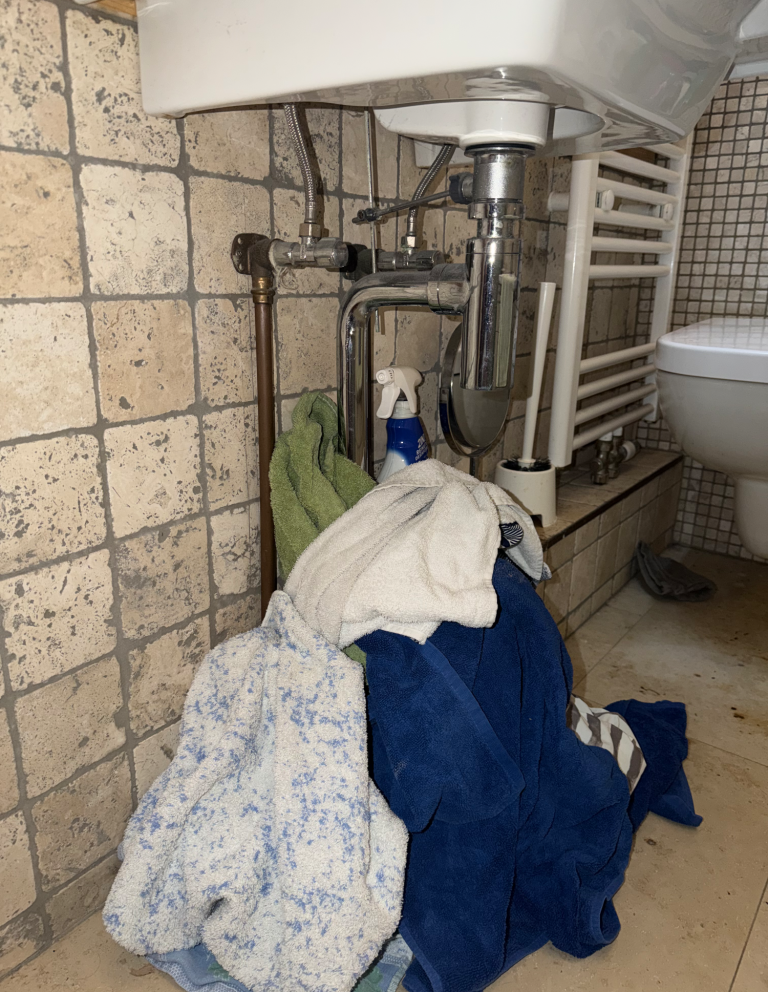 Handtücher unter einem undichten Waschbecken im Badezimmer ausgelegt, um austretendes Wasser provisorisch einzudämmen