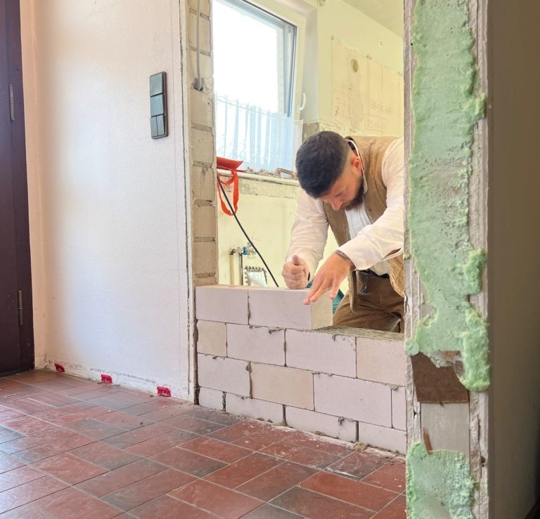 Maurer verschließt eine Wandöffnung mit Kalksandstein-Steinen in einem Wohnhaus; fachgerechtes Zumauern einer alten Tür.