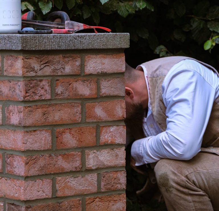 Maurer führt die letzten Arbeitsschritte an einer neu gemauerten Klinker-Säule aus; finale Ausbesserungen und Kontrolle der Fugen